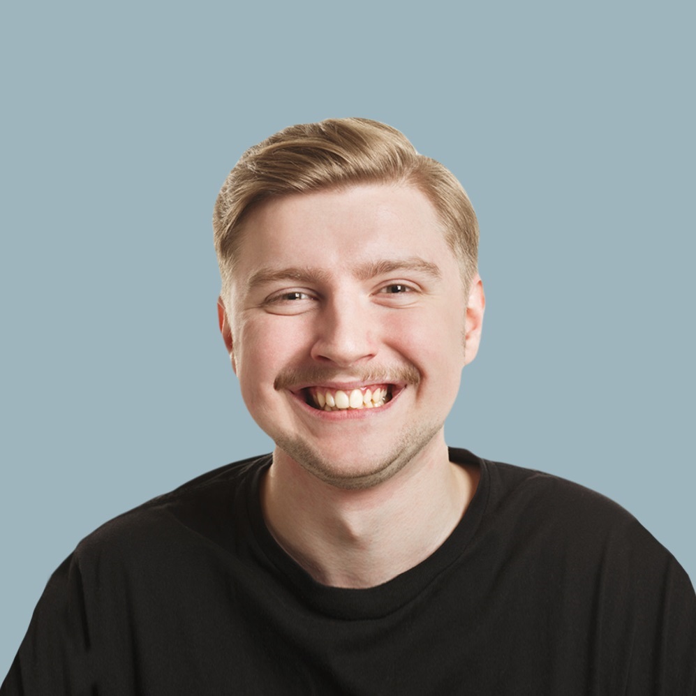 Smiling man with short light hair wearing a black T-shirt against a light blue background, facing the camera.