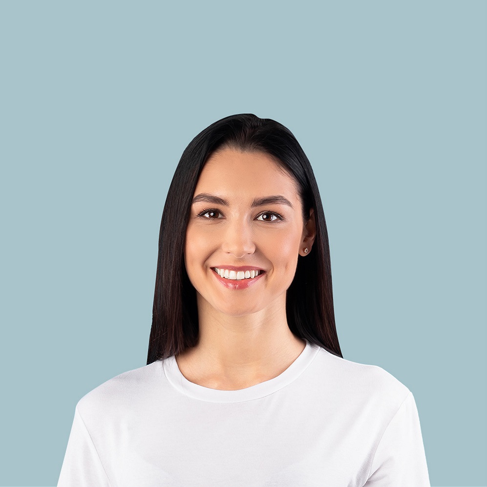 Smiling woman with long dark hair wearing a white T-shirt against a light blue background, facing the camera.